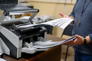 A photo of a person removing ballots from a scanner that have been scanned already.